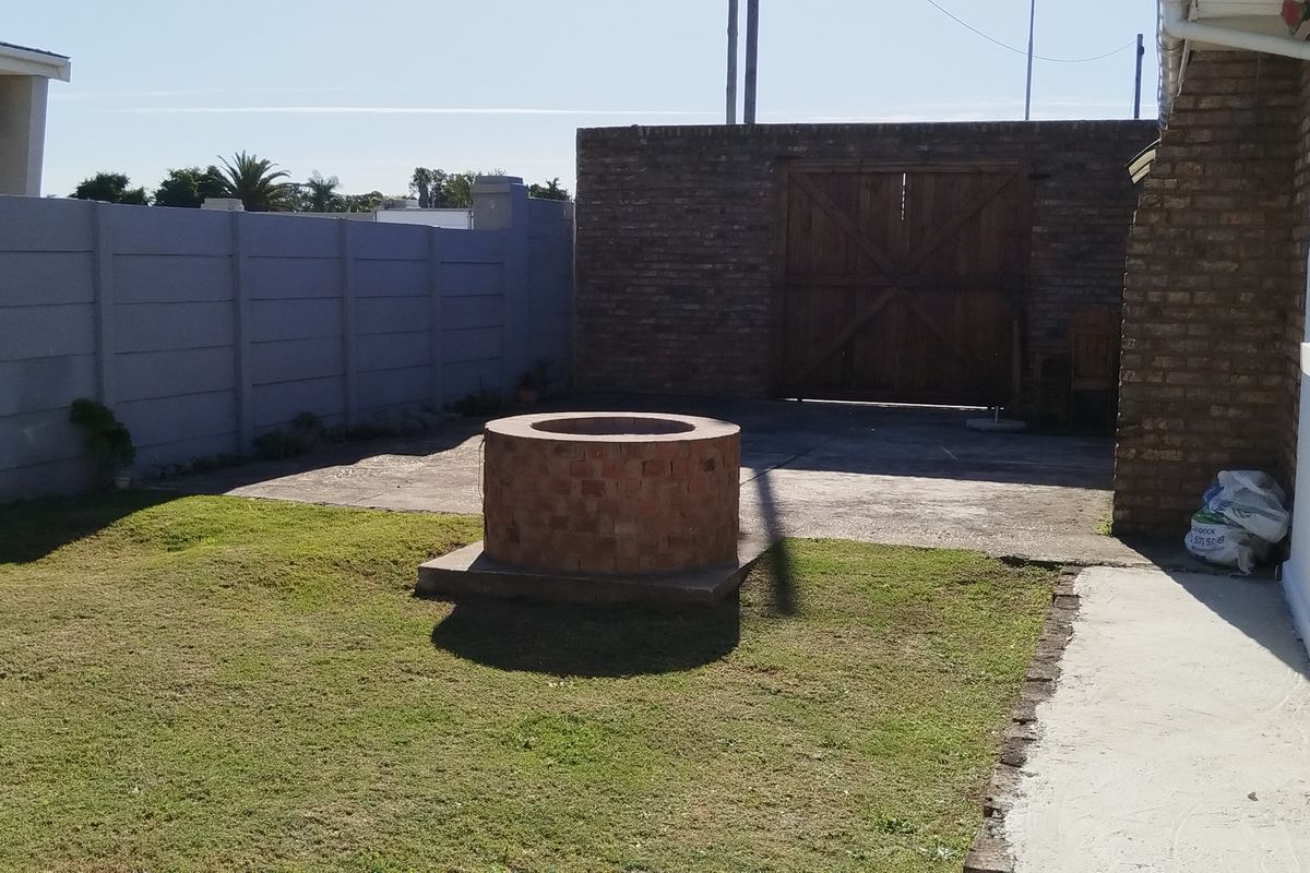 Rear garden area featuring a circular brick fire pit, concrete patio space, and perimeter walling.