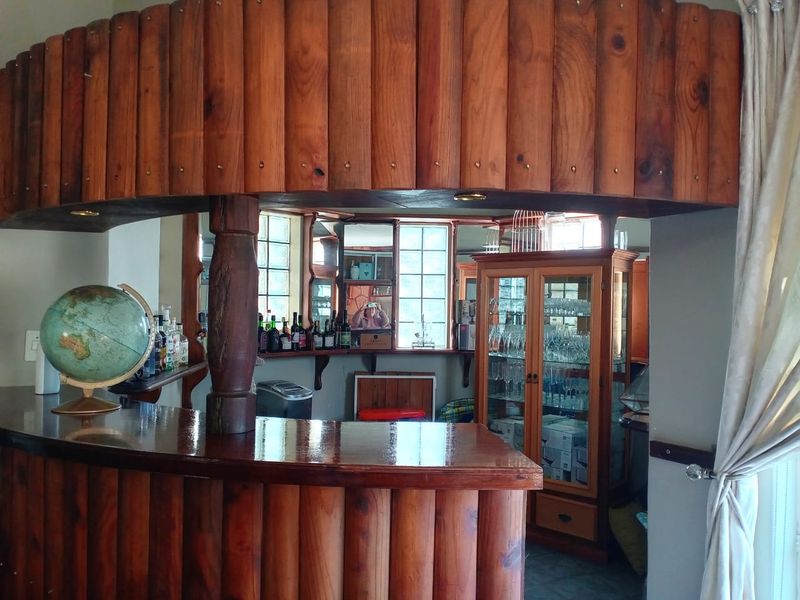 A dedicated home bar area featuring a custom wooden bar counter, overhead canopy, mirrored back bar, and built-in display cabinetry with leaded glass windows.