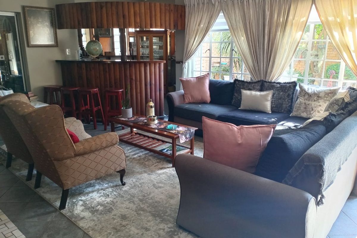 A spacious living room featuring a built-in wooden bar area, tiled flooring, and large windows that provide ample natural light.