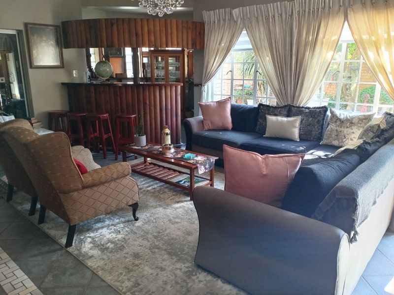 A spacious living room featuring a built-in wooden bar area, tiled flooring, and large windows that provide ample natural light.