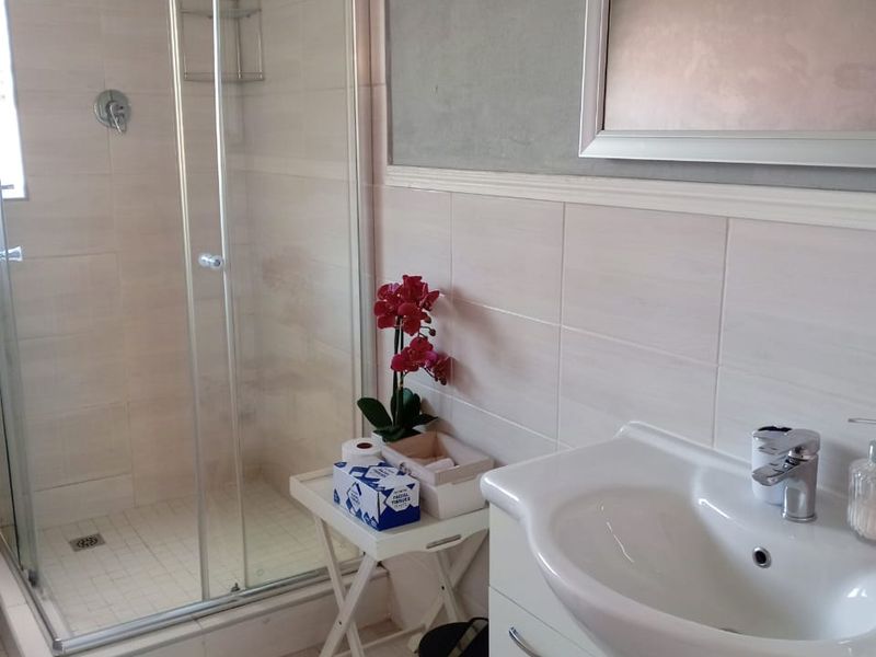 A clean, modern bathroom featuring a glass shower enclosure, a white vanity cabinet with a basin, and neutral wall and floor tiling.