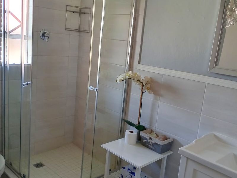 A well-maintained bathroom featuring a glass shower enclosure, tiled finishes, and a modern vanity cabinet, complemented by a decorative chandelier.