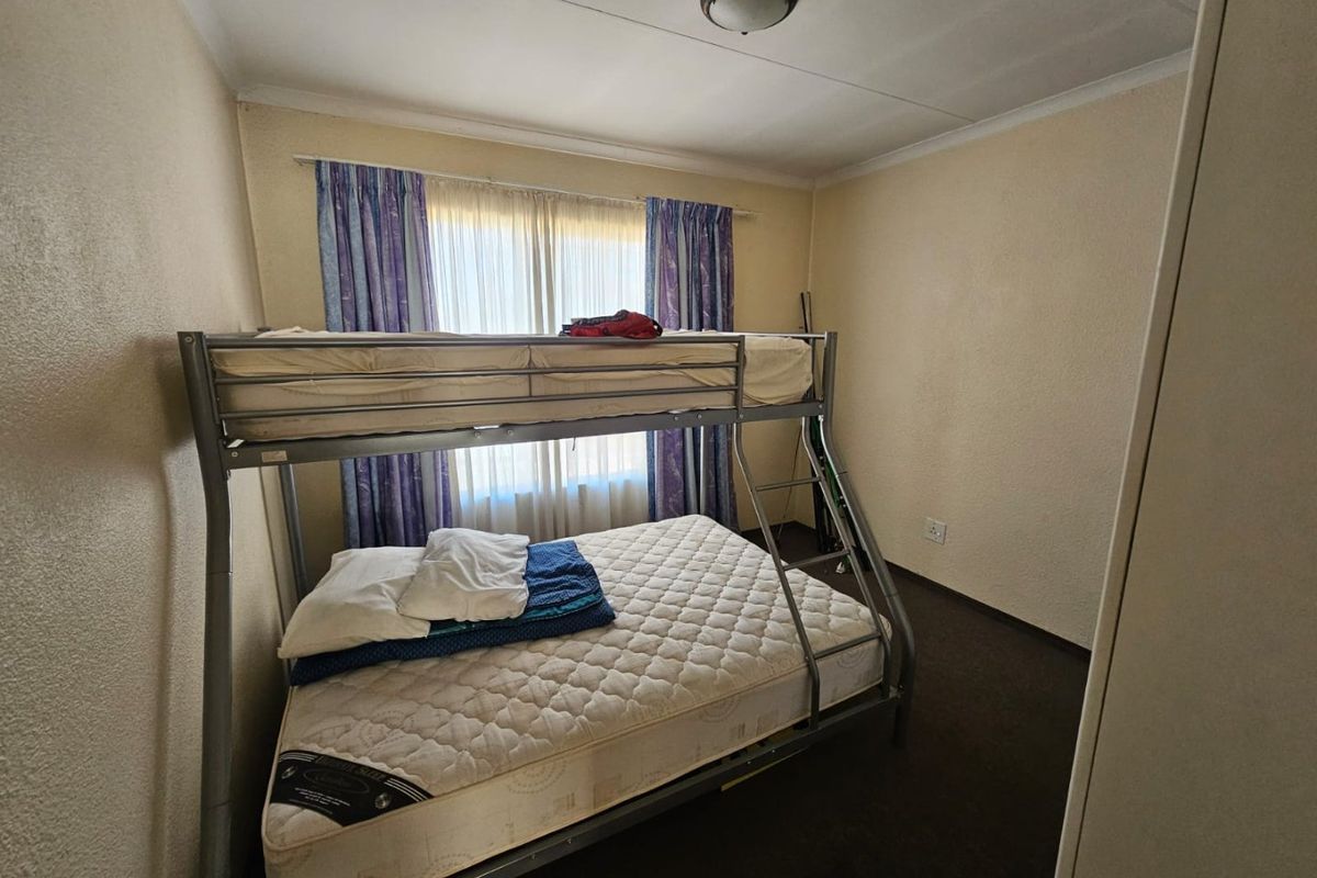 A functional bedroom featuring carpeted flooring, a built-in cupboard, and a window with curtain tracks.