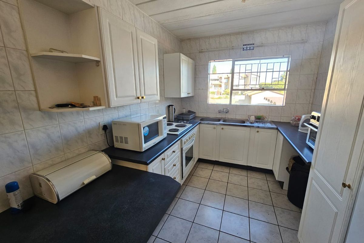 A functional kitchen featuring white cabinetry, dark countertops, a built-in oven with hob, and a double sink with a window view.