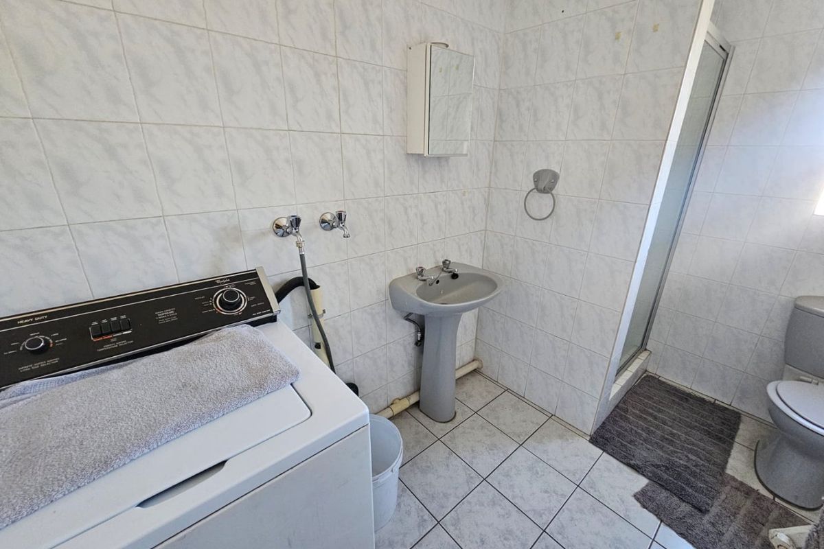 A functional bathroom and laundry area featuring a pedestal basin, toilet, shower enclosure, and dedicated space for a washing machine.