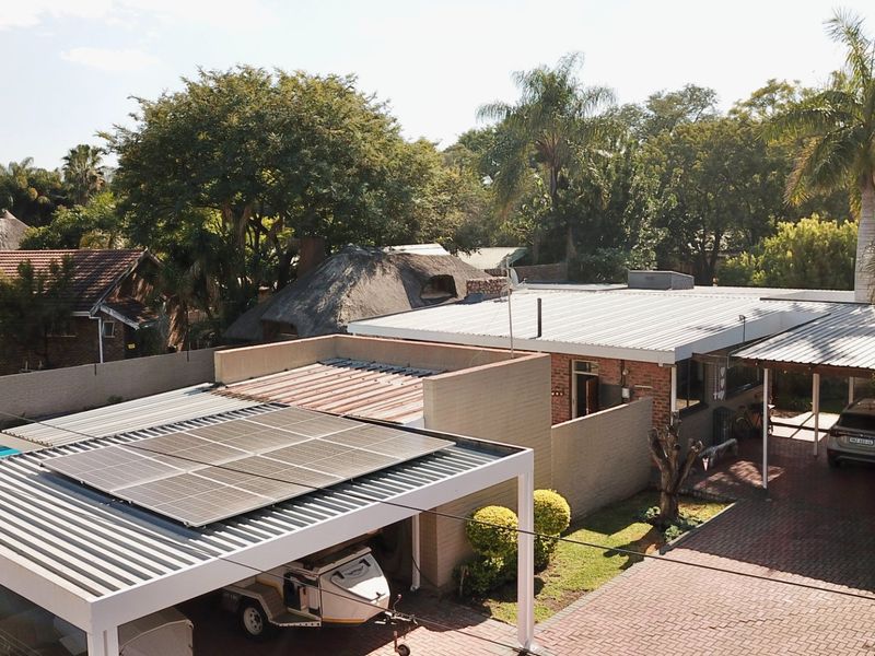 Aerial view of the property featuring a paved driveway, carport, solar panel installation, and a swimming pool in a landscaped residential setting.