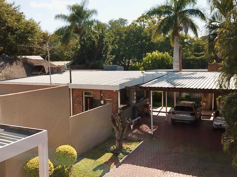 Aerial view of a residential property featuring a brick facade, corrugated metal roofing, a paved driveway, and a covered carport area.