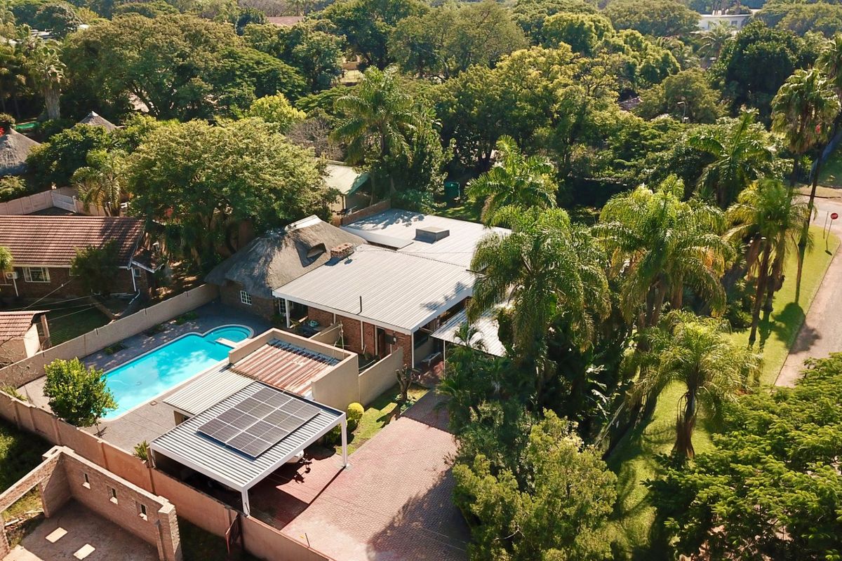 Aerial view of a residential property featuring a swimming pool, solar panels, paved driveway, and a mix of thatched and metal roofing.