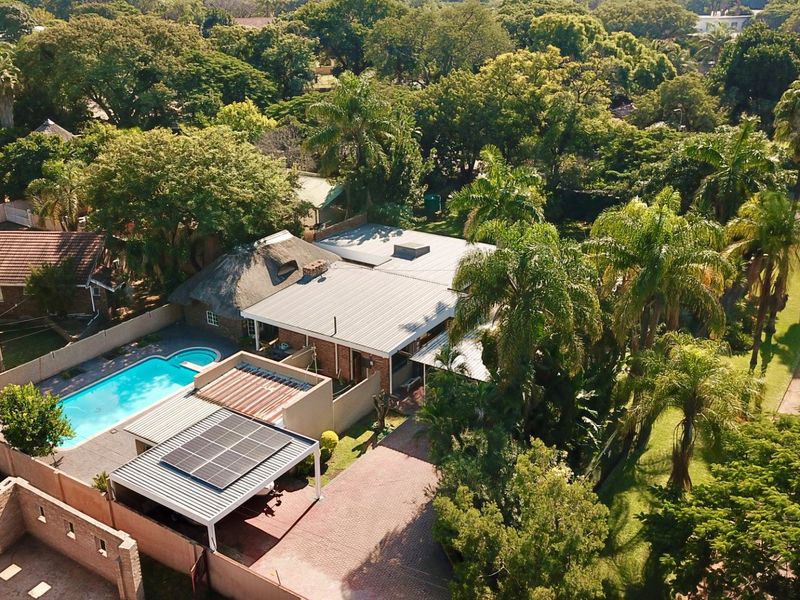 Aerial view of a residential property featuring a swimming pool, solar panels, paved driveway, and a mix of thatched and metal roofing.
