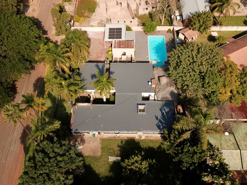 Aerial view of the property featuring a swimming pool, solar panels on the roof, and established garden surroundings.