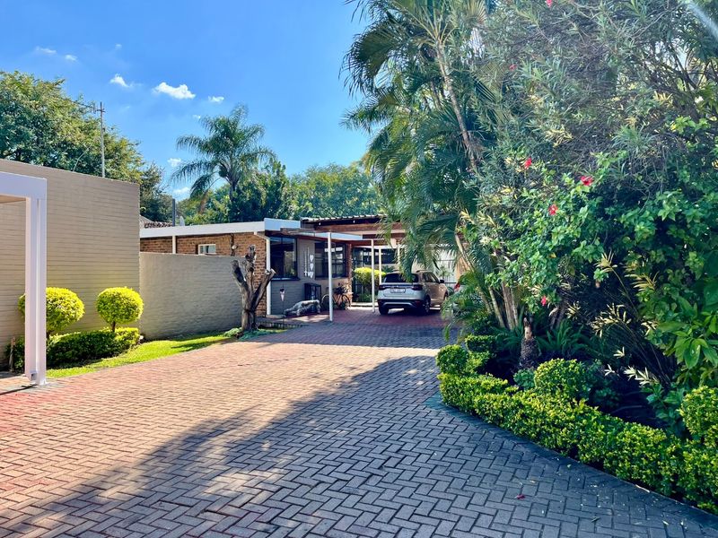 Front view of the property featuring a paved driveway, established garden, and a covered carport area.