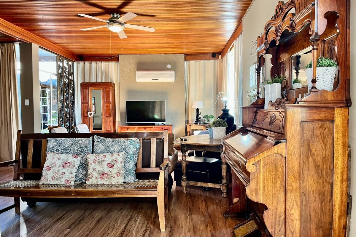 A cozy living room featuring a warm timber-paneled ceiling, ceiling fan, split-system air conditioning, and durable laminate flooring.