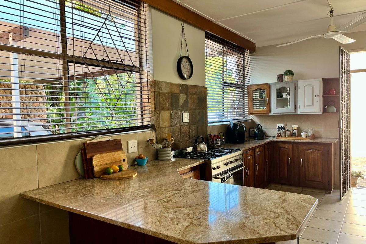 A functional kitchen featuring granite countertops, wooden cabinetry, a gas hob with oven, and a tiled backsplash, offering ample workspace and natural light.