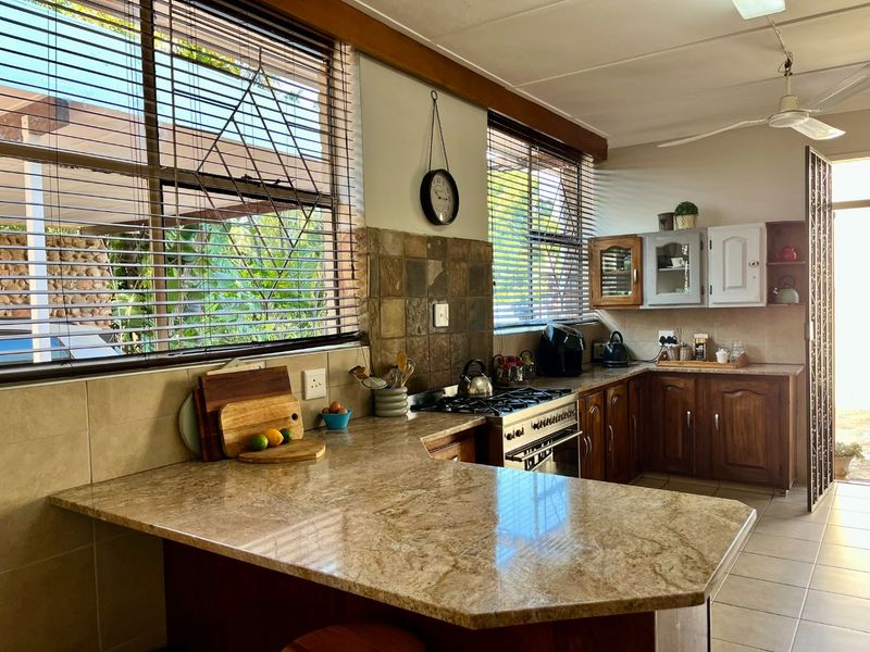 A functional kitchen featuring granite countertops, wooden cabinetry, a gas hob with oven, and a tiled backsplash, offering ample workspace and natural light.