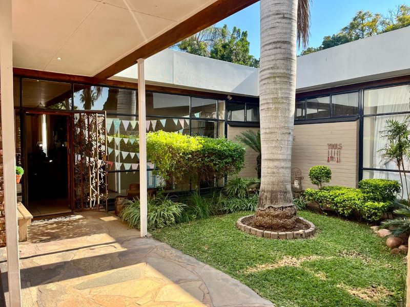 A covered patio area featuring stone paving and a view into a central courtyard garden with established landscaping and large glass window panels.