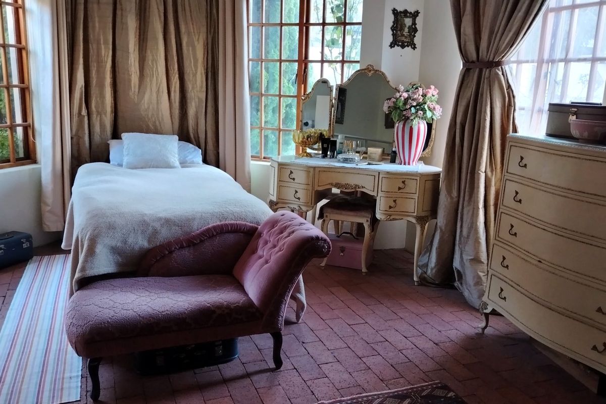 A bedroom featuring terracotta tile flooring and large windows with wooden frames, providing natural light and garden views.
