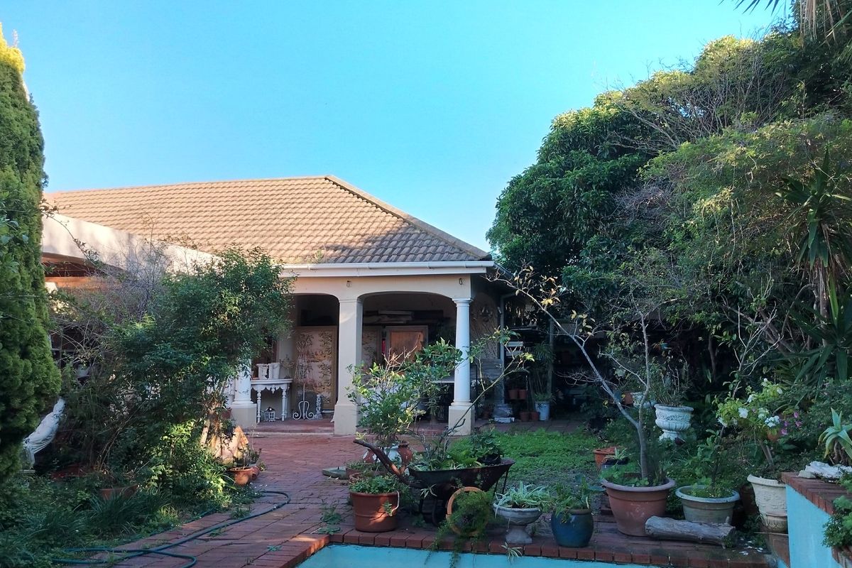 A rear view of the house featuring a covered patio with classic columns, overlooking a garden area with established trees and paved pathways.