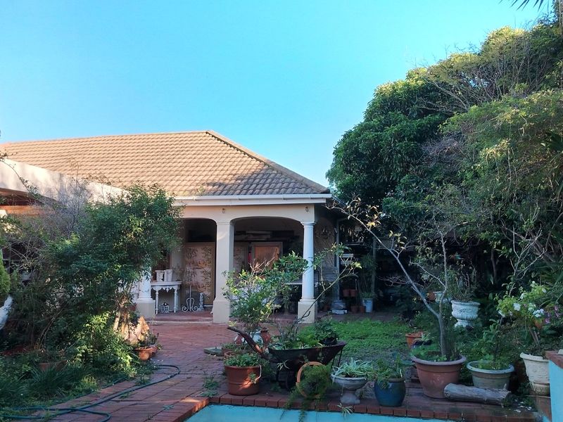 A rear view of the house featuring a covered patio with classic columns, overlooking a garden area with established trees and paved pathways.