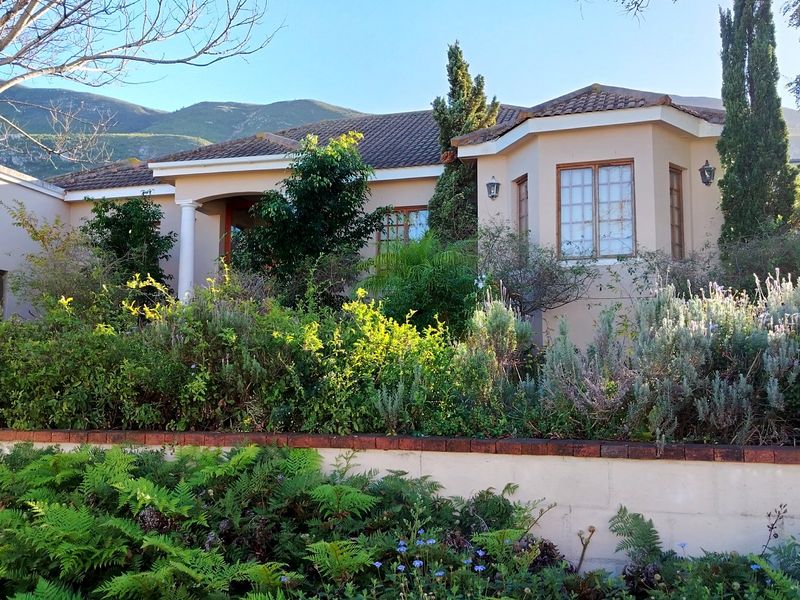 A charming single-story residence featuring a tiled roof, classic architectural details, and a lush, established front garden with mountain views.