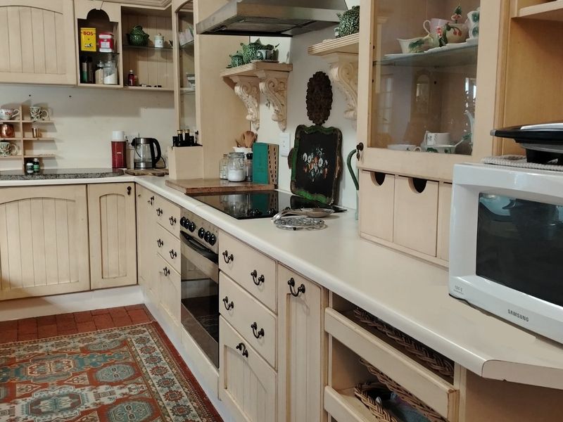 A traditional kitchen featuring cream-colored cabinetry, a built-in oven, a glass cooktop, and an extractor fan with decorative shelving.