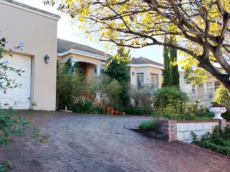 Front elevation of the house featuring a paved driveway, single garage, and established garden with mature trees.