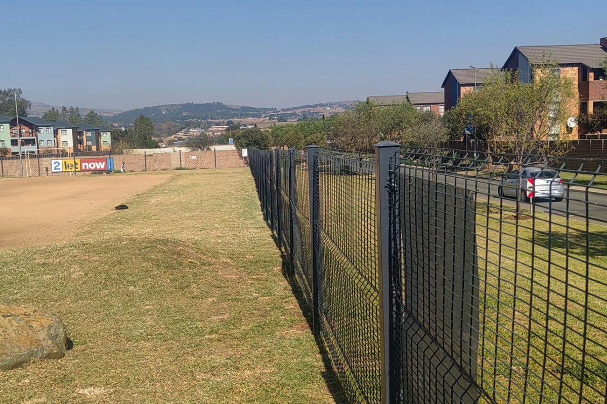 View of the apartment complex grounds featuring secure perimeter fencing, manicured lawn areas, and adjacent paved access road.