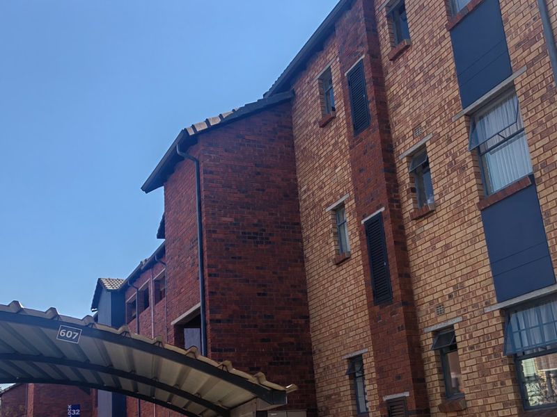 Exterior view of a multi-story apartment building featuring face brick construction and a covered carport area.