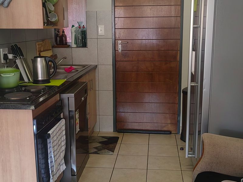 A functional kitchen featuring built-in cabinetry, laminate countertops, a tiled backsplash, and a solid wood door leading to the exterior.