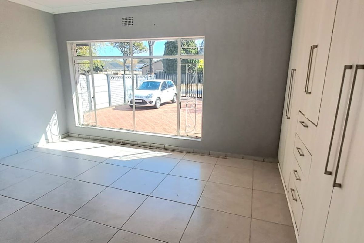 A bright, empty bedroom featuring neutral tiled flooring and ample built-in cupboard storage, with large windows overlooking the front driveway.