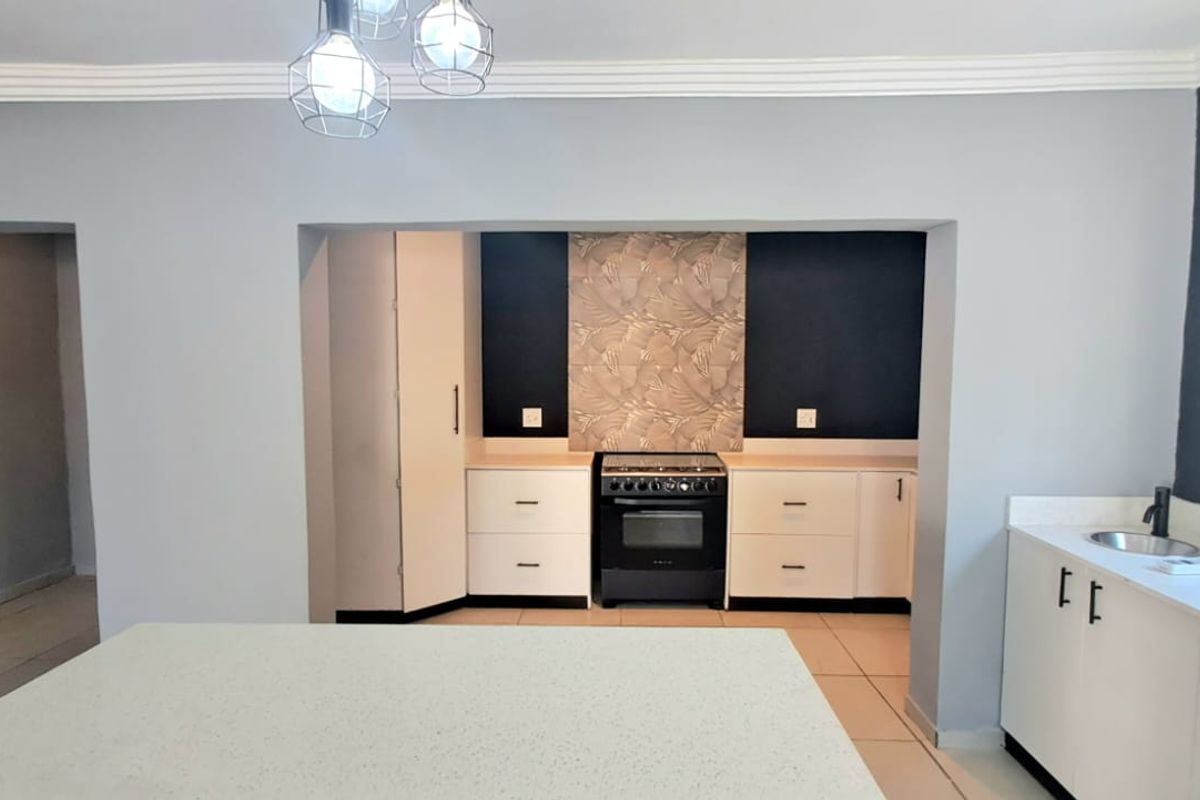 Modern kitchen featuring white cabinetry, stone countertops, a freestanding stove, and a neutral color palette with decorative feature wall accents.