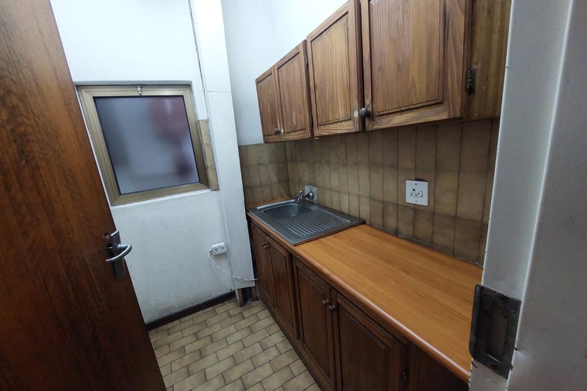 A compact office kitchenette featuring wooden cabinetry, a stainless steel sink, and tiled splashbacks.