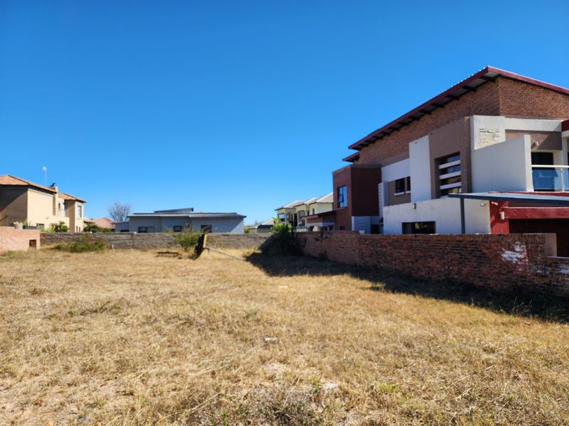 A vacant residential plot featuring a brick boundary wall and views of adjacent modern housing developments.