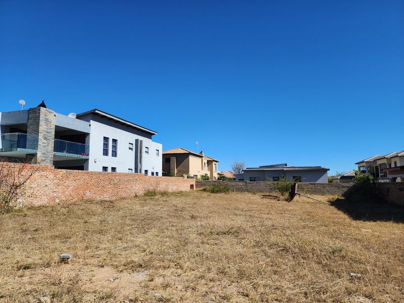 A vacant residential plot featuring established brick and stone boundary walls, situated within a developed neighborhood setting.