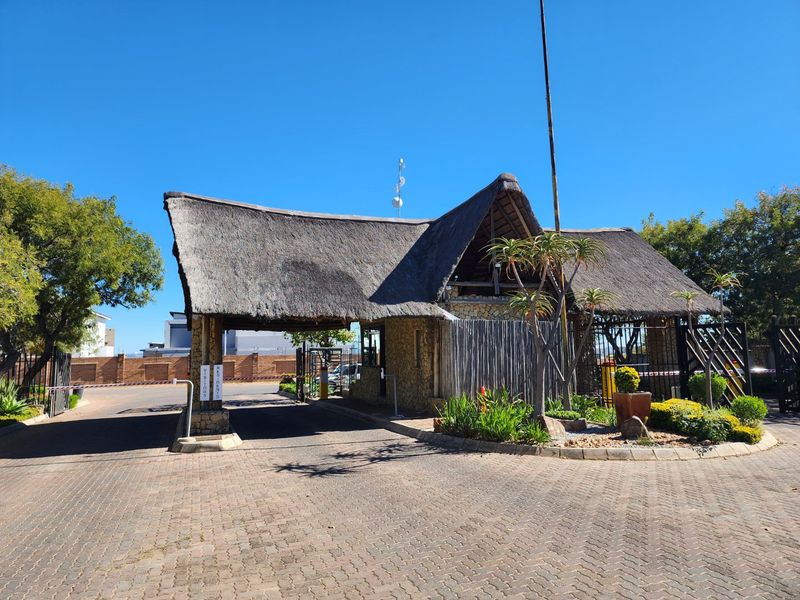 A secure gated entrance to the residential estate featuring a traditional thatched roof structure, paved driveway, and controlled access boom gates.