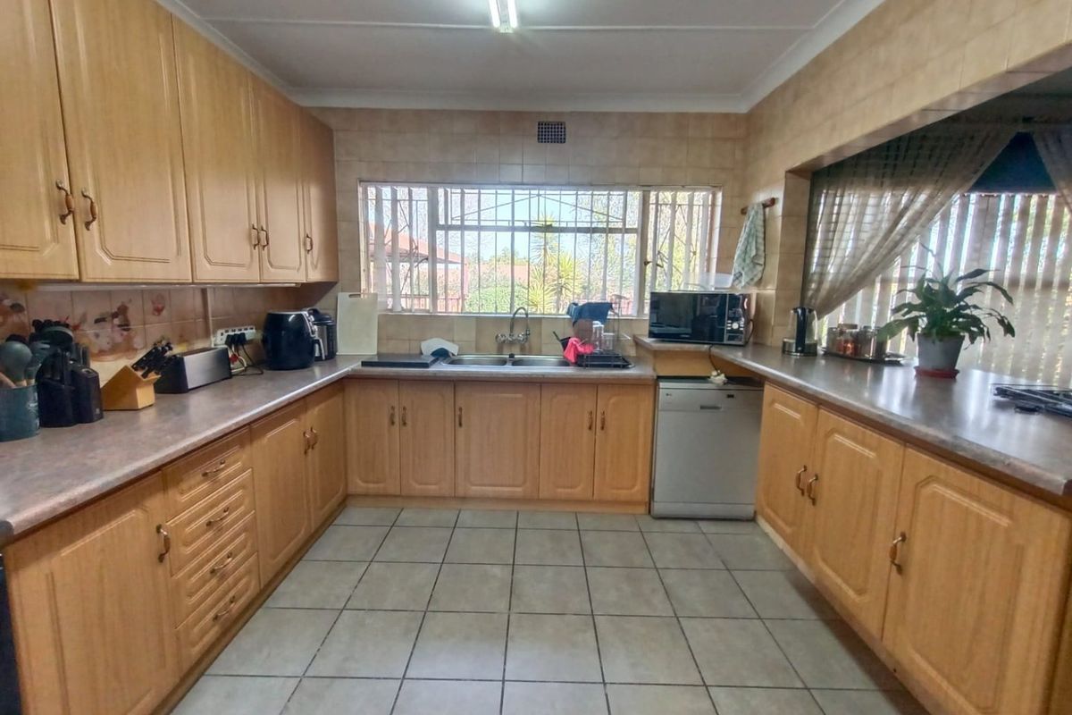 A functional kitchen featuring U-shaped wooden cabinetry, tiled flooring, and a double basin sink with a window view.