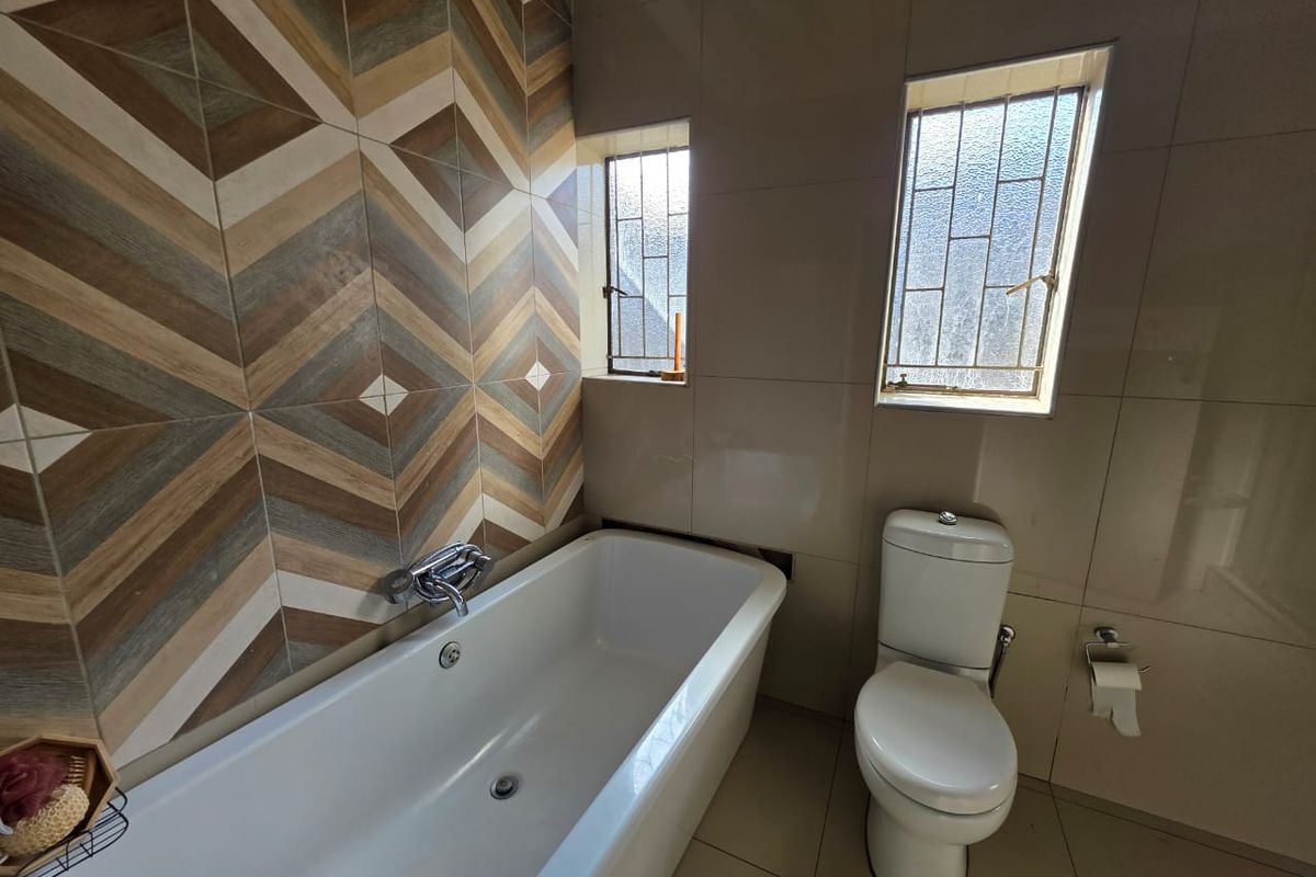 A modern bathroom featuring a white bathtub with chrome fixtures, a dual-flush toilet, and decorative geometric wall tiling.