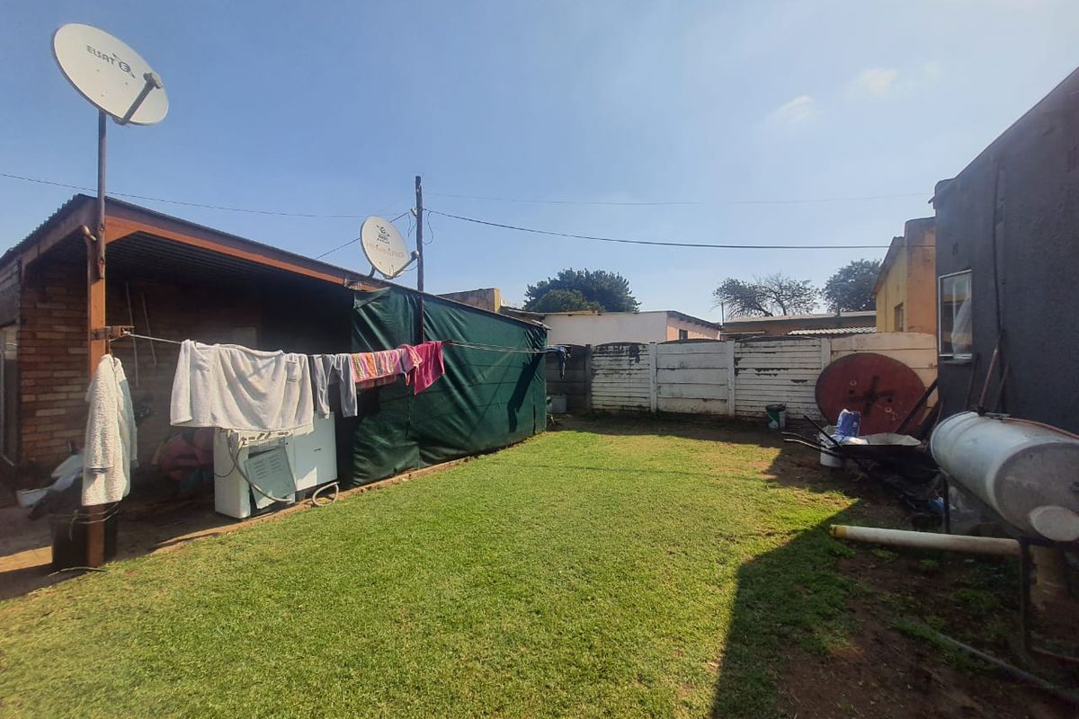 A rear garden area featuring a lawn, perimeter boundary walls, and a covered outdoor utility space with satellite dish infrastructure.