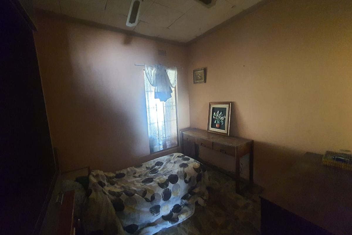 A bedroom featuring a ceiling fan, window with security bars, and dated interior finishes.