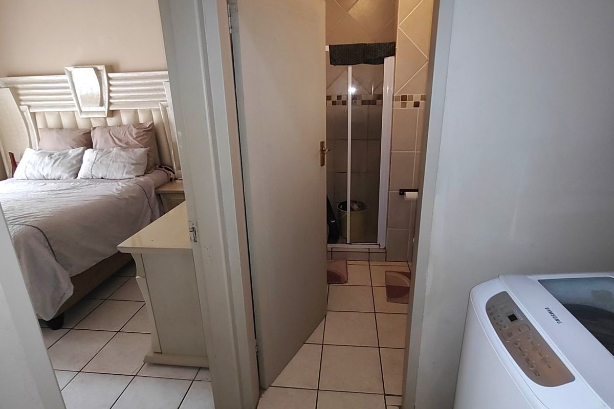 A view showing a bedroom with tiled flooring and an adjacent bathroom featuring a shower enclosure, with a laundry area visible in the foreground.