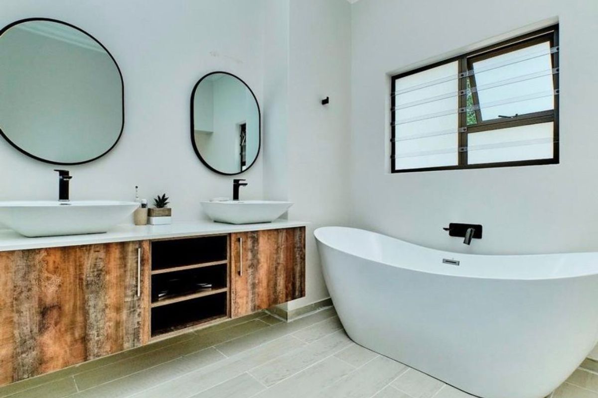 Modern bathroom featuring a floating wood-finish vanity with dual vessel sinks, a freestanding bathtub, and contemporary black fixtures.