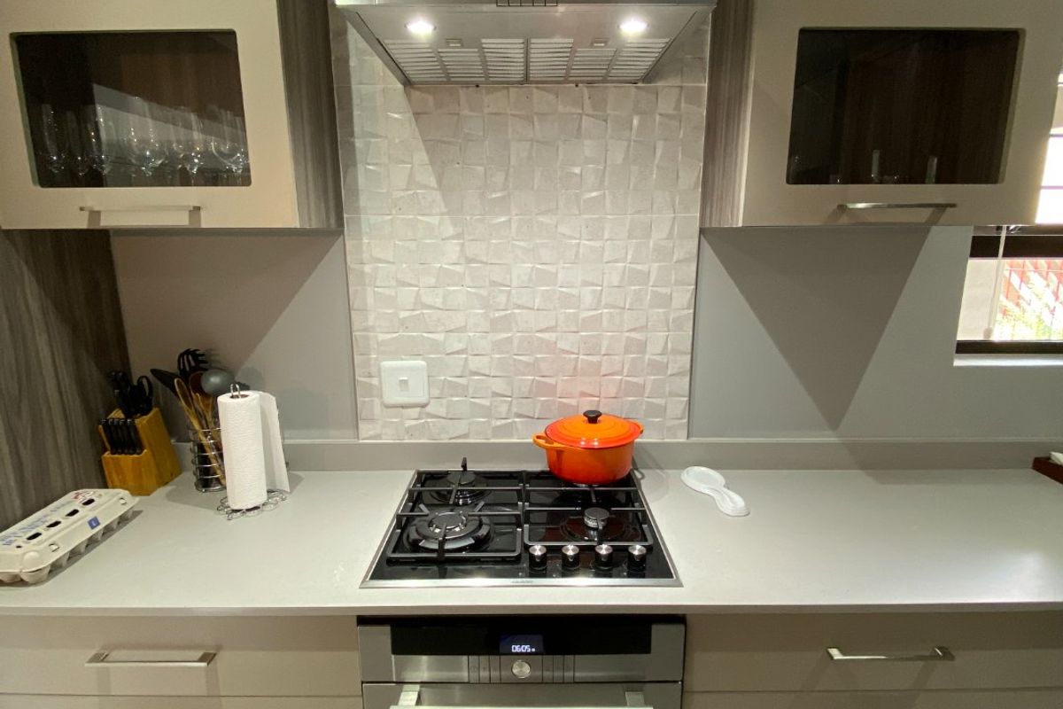Modern kitchen featuring built-in cabinetry, stone countertops, a gas hob, integrated oven, and a stainless steel extractor fan with textured tile splashback.