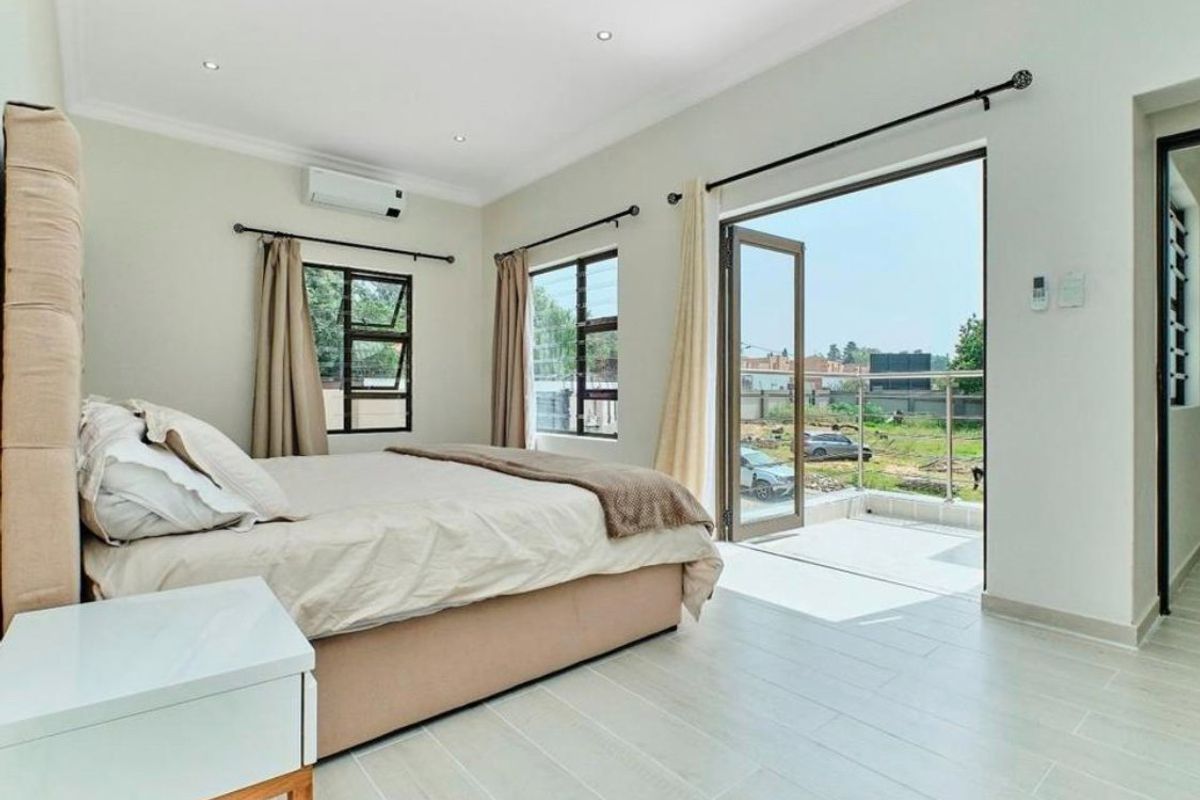 Bright bedroom featuring tiled flooring, recessed lighting, a wall-mounted air conditioning unit, and direct access to a private balcony through glass doors.