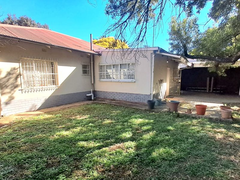 Rear view of the property featuring a paved patio area, security bars on windows, and a corrugated metal roof.