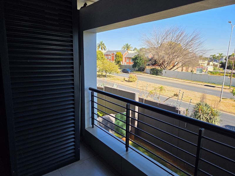 A clean, covered balcony featuring tiled flooring, a modern metal balustrade, and a sliding shutter screen, offering an open view of the street.