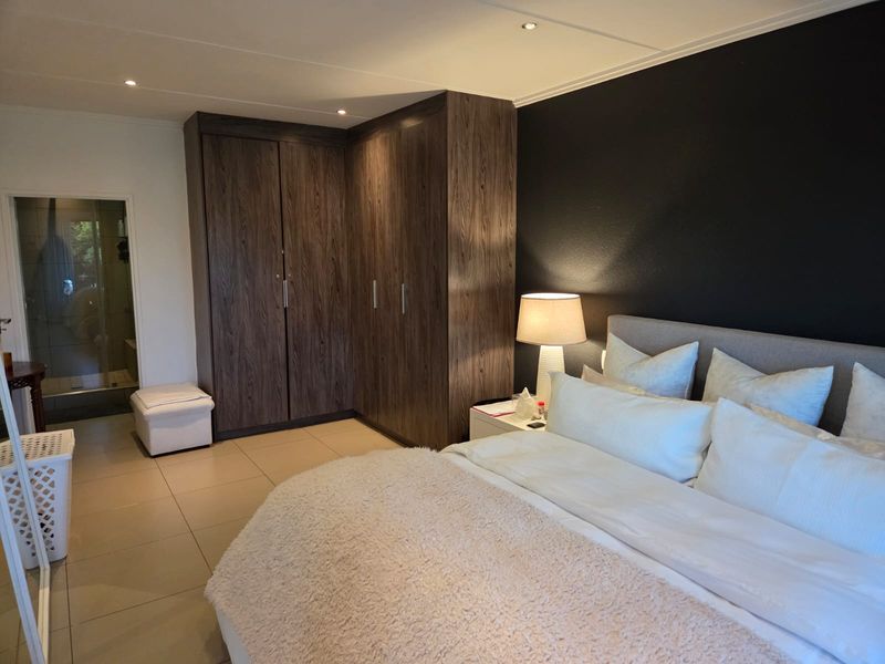 A well-maintained bedroom featuring dark wood built-in cupboards, tiled flooring, recessed lighting, and direct access to an en-suite bathroom.