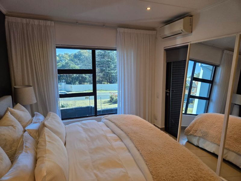 A well-maintained bedroom featuring tiled flooring, an integrated air conditioning unit, and large aluminium-framed windows providing natural light.
