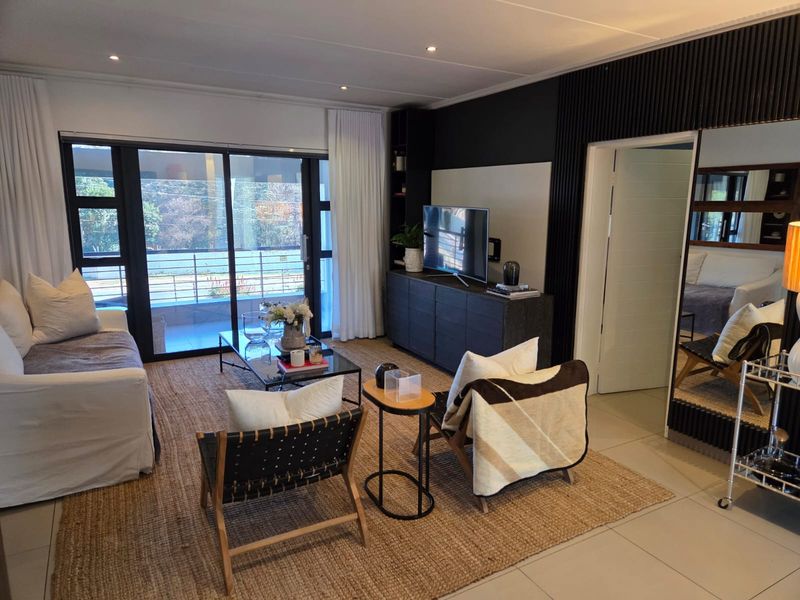 Modern living room featuring tiled floors, recessed lighting, and a stylish dark feature wall with integrated shelving and sliding doors leading to a balcony.