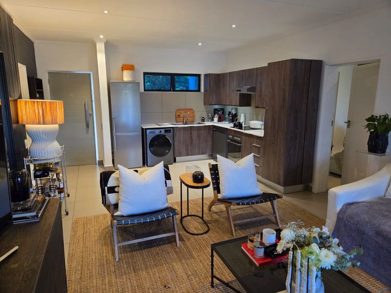 Modern open-plan living area featuring a well-appointed kitchen with dark wood cabinetry, integrated appliances, and sleek tiled flooring throughout.