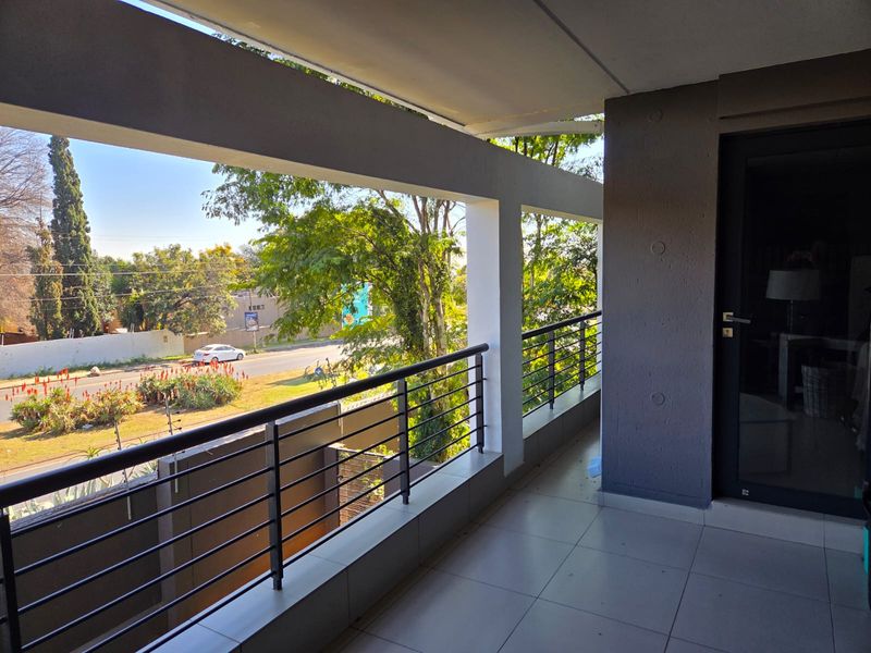 A covered balcony featuring tiled flooring, a modern metal balustrade, and views over the surrounding street and greenery.