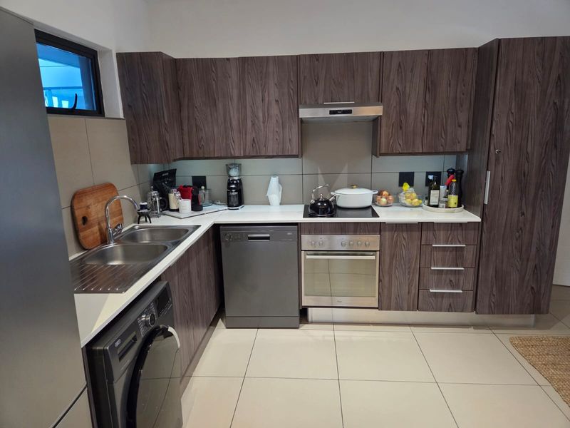 Modern kitchen featuring dark wood-grain cabinetry, stone-look countertops, tiled backsplash, and integrated stainless steel appliances including an oven and hob.